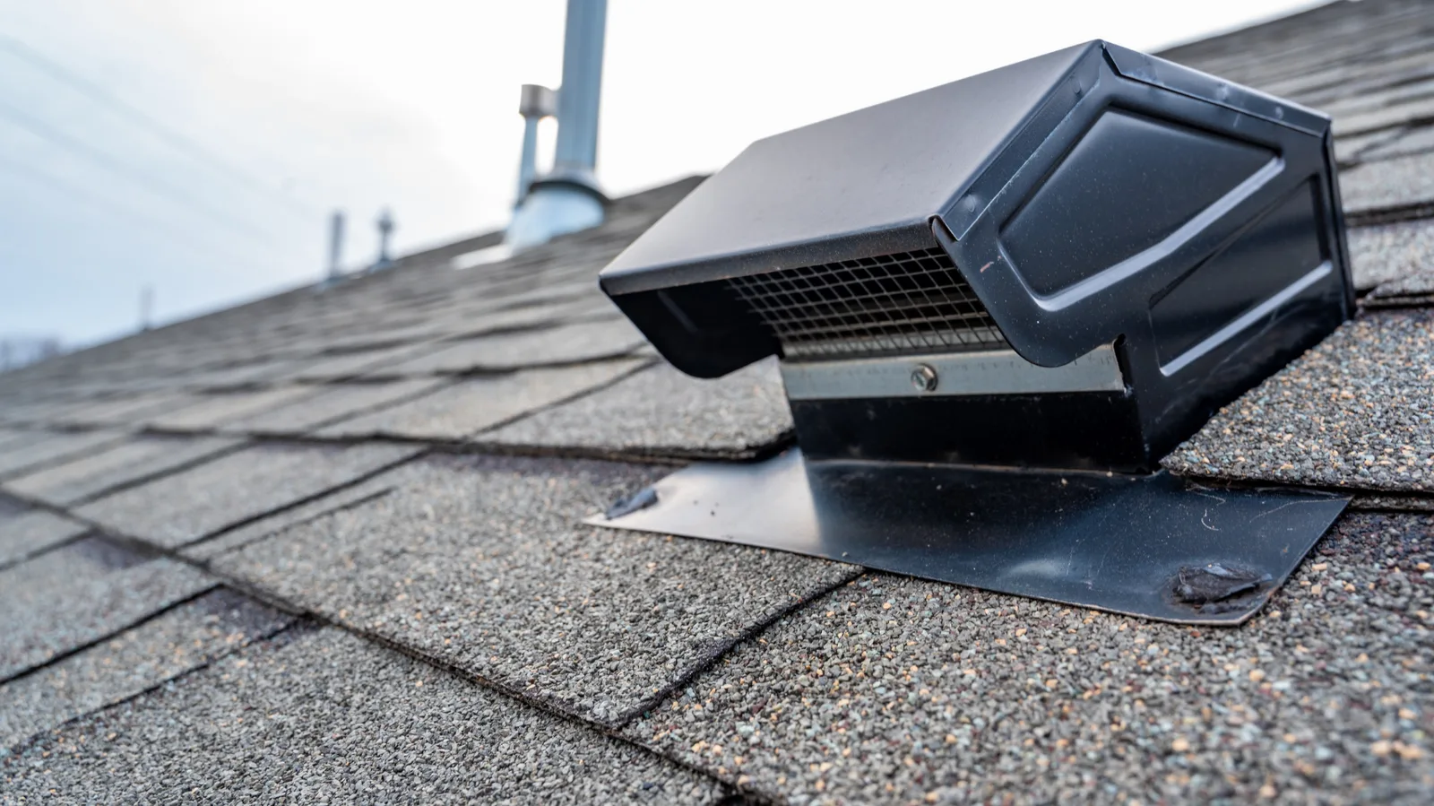 Black roof vent cap mounted on shingles with metal flashing
